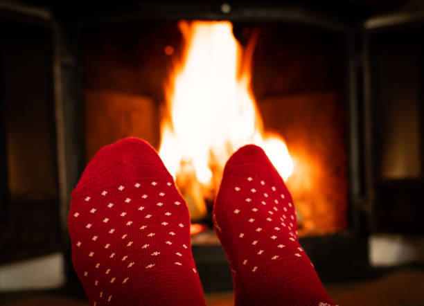 istock Female feet in red woolen socks by a warm fireplace on a cold winters evening. Shallow depth of field. 1299133371