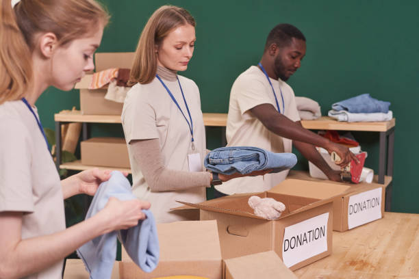 istock Group of modern multi-ethnic volunteers sorting and  packing clothes into cardboard boxes for donation, medium shot 1299134300