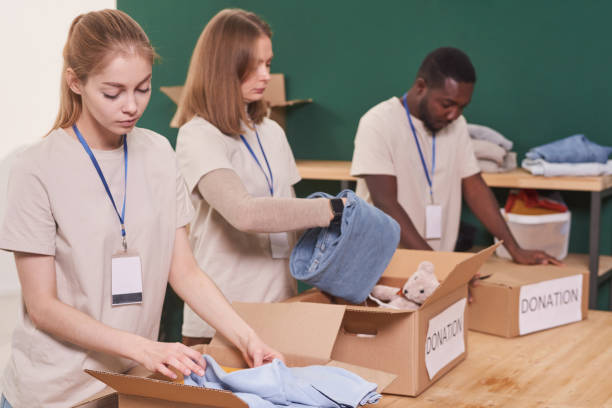 istock Group of modern charity volunteers packing clothes into cardboard boxes for donation, medium shot 1299134305