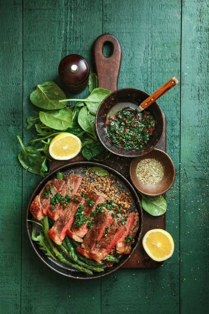Spicy grilled Ribeye steak with salsa verde, asparagus, quinoa and lentil salad. Flat lay top-down composition on dark green background.
