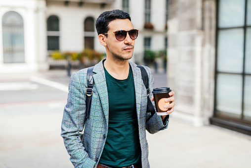 Latino man walking down the streets of London, UK, with coffee cup