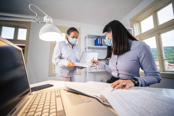 istock The New Normal. New office setup. Two colleagues wearing protective face masks working together in the office while COVID-19 pandemic. 1299136606