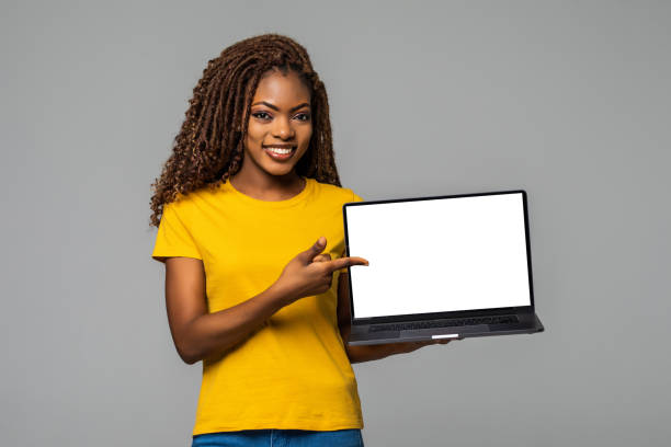 istock Young smiling african woman standing with laptop computer isolated on gray background 1299136866