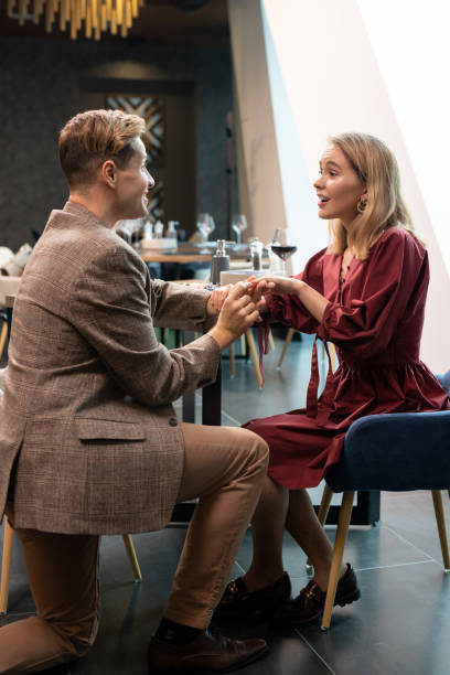 istock Guy looking at surprised girlfiend while putting engagement ring on her finger 1299137710