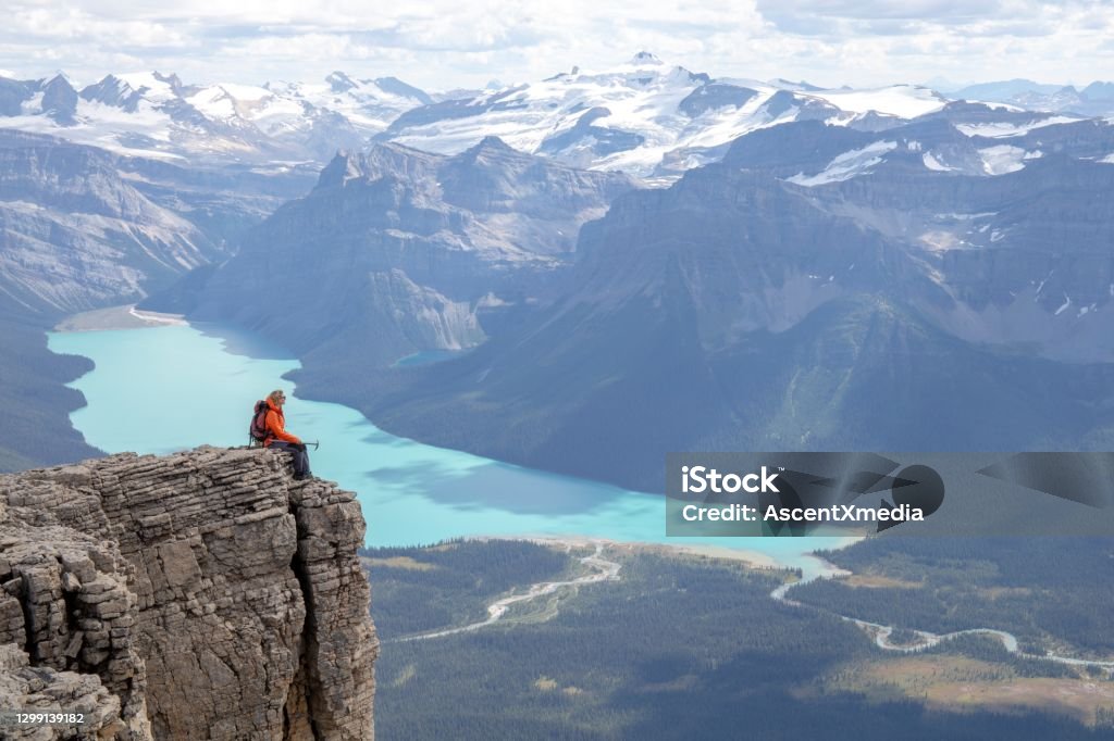 Female mountaineer relaxes on mountain ridge in the morning Hector Lake and Canadian Rockies visible in the distance Canada Stock Photo