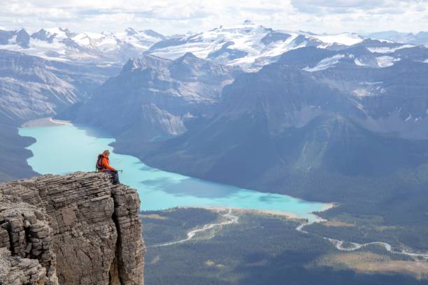 Female mountaineer relaxes on mountain ridge in the morning Hector Lake and Canadian Rockies visible in the distance rocky mountains north america photos stock pictures, royalty-free photos & images
