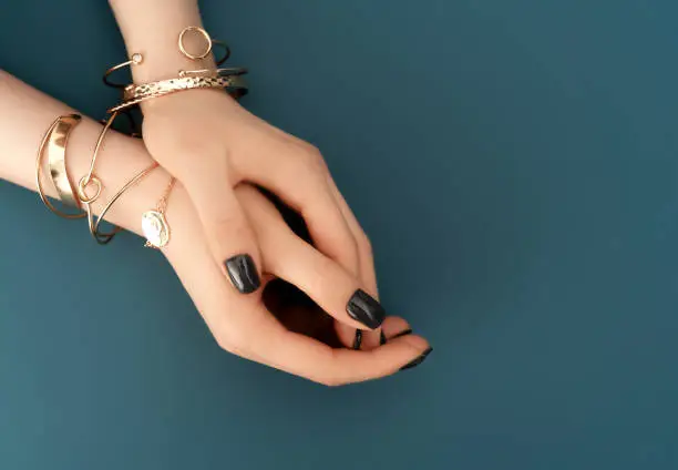 Female hands with trendy dark nail design with gold bracelets on aqua background. Luxury concept. Festive backdrop for your design. Top view.