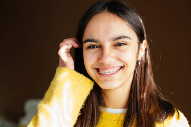 Cute and happy teen girl with braces smiling to camera Portrait of a happy teen girl with braces and some acne smiling at home with the sun coming through the window 12 13 years photos stock pictures, royalty-free photos & images