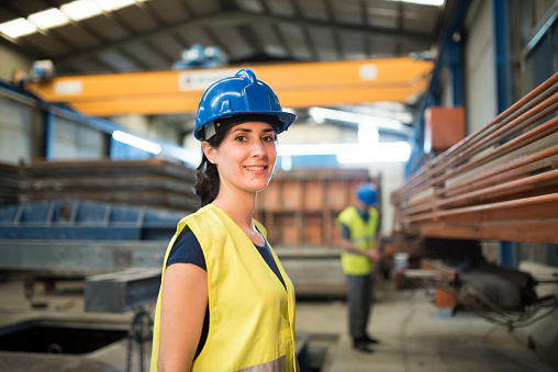 Pretty construction worker woman in factory looking smiling at camera
