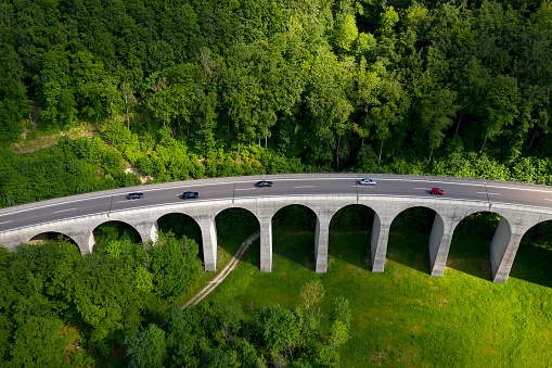 Traffic on a highway arch bridge over green forest, viewed from above.