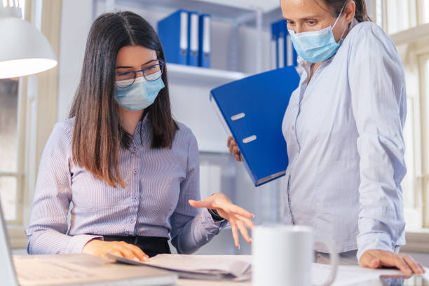 istock The New Normal. New office setup. Two colleagues wearing protective face masks working together in the office while COVID-19 pandemic. 1299143706