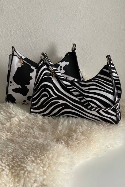 Woman’s cow and zebra printed little black and white bags lying on beige fur. Style and fashion. Accessories