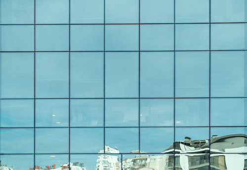 Full frame photo of modern glass wall of building with city buildings and sky reflection seen on. Shot with a full frame mirrorless camera.