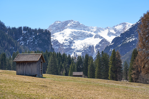 Log cabin and snowcapped Dolomite mountain in the background.