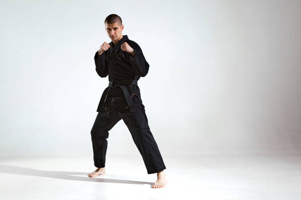 istock Confident guy in black kimono fighter posing in karate stance on studio background with copy space, mix fight concept 1299149714