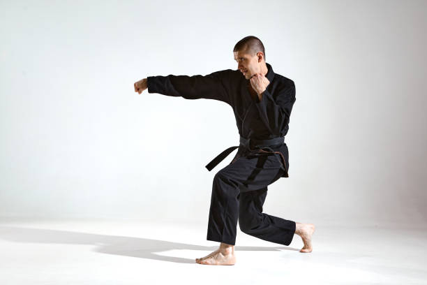 istock Fighting guy in black kimono fighter demonstrating karate technique on studio background with copy space 1299149749