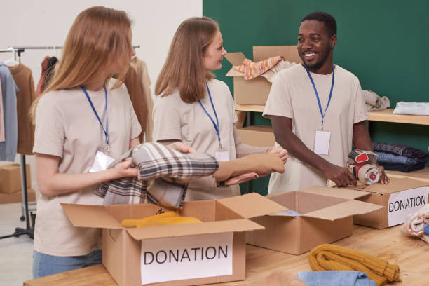 istock Group of three joyful volunteers talking about funny things while packing new clothes for donation 1299150551