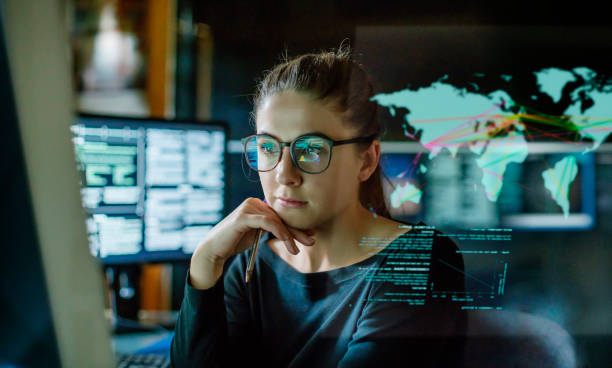 Young woman global communications Stock image of a young woman, wearing glasses, surrounded by computer monitors in a dark office. In front of her there is a see-through displaying showing a map of the world with some data. finance technology stock pictures, royalty-free photos & images