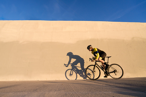 Young Competitive Road Cyclist riding along a bike path at sunset with this shadow casting.