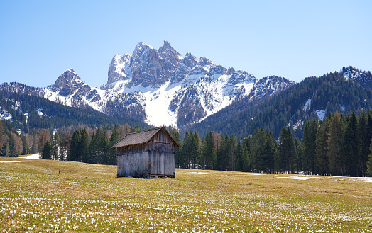 Log cabin and snowcapped Dolomite mountain in the background.