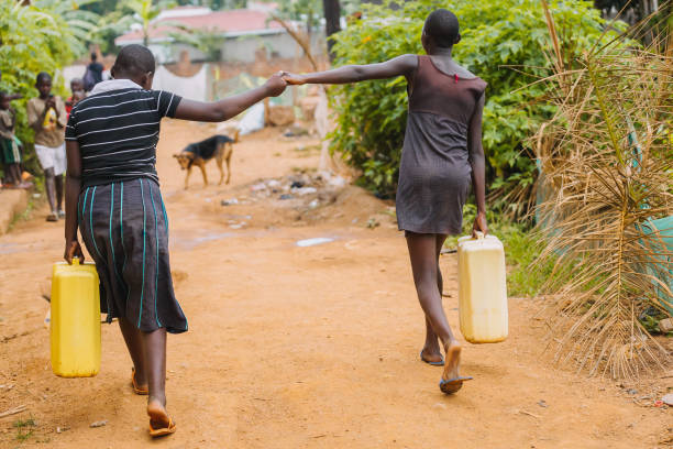 Two women holding hands while carrying water cans in Uganda, Africa Two women holding hands while carrying water cans after fetching water from the public well in Entebbe, Uganda uganda stock pictures, royalty-free photos & images