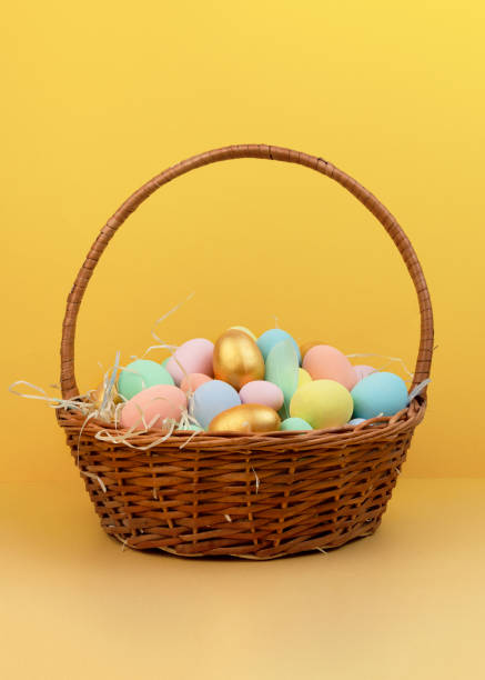 istock Wicker basket with colorful Easter eggs in pastel colors on yellow background 1299154802