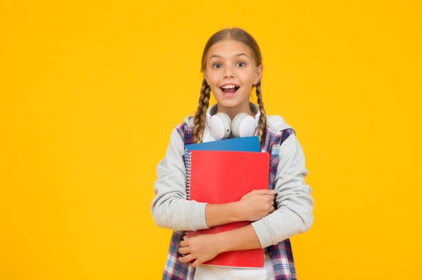 istock small happy kid in earphones with notepad. child ready to learn subject. back to school. Study lessons for exam. feel the great surprise. knowledge day. surprised pupil yellow background, copy space 1299157204
