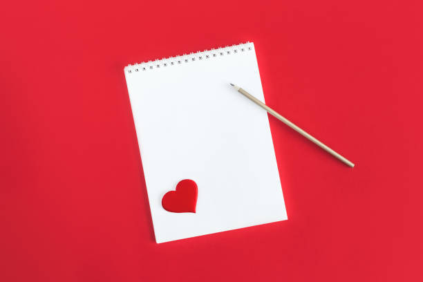 istock Notebook with blank page, pencil and red heart on a red background. 1299157292