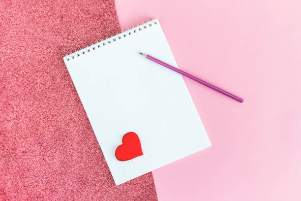 istock Notebook with blank page, pencil and red heart on a pink background. 1299157299