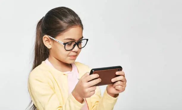 Smartphone use, cause eye damage for children. Child wearing eyeglasses looks at smartphone