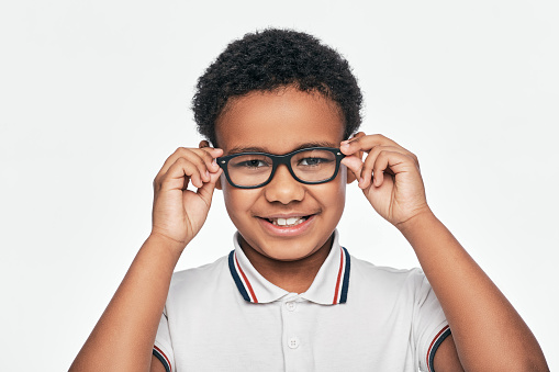 African American little boy adjusting stylish eyeglasses, looking at camera, isolated on white background