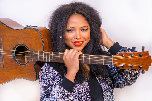 A closeup of a young smiling Hispanic female posing at the camera holding a guitar on her shoulder on a white background