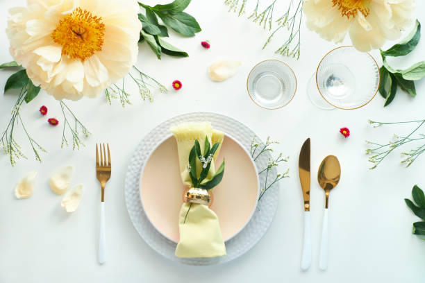 istock Effortless golden birthday dinner table decor. Pale yellow peony flowers. White dinner table, white and gold utensils, decorated with season flowers and palm leaves 1299159938