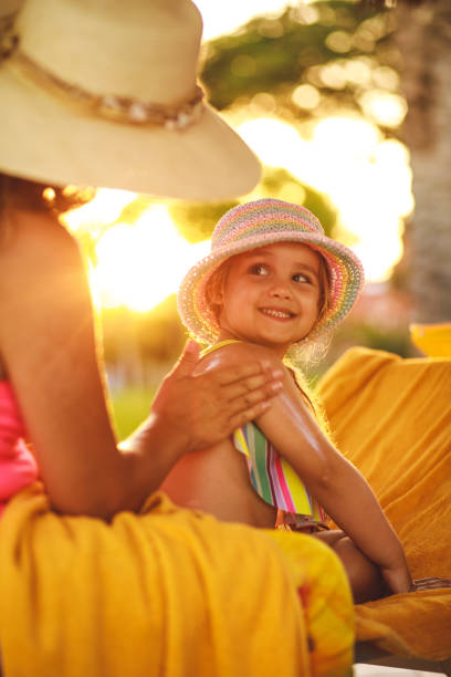 petite fille souriant à sa mère tandis qu’elle applique l’écran solaire sur son dos - outdoor chair furniture travel vacations photos et images de collection