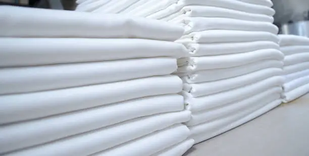 Stacks of folded white fabrics or sheets in a laundry. Cleaning service for institutions and industries.