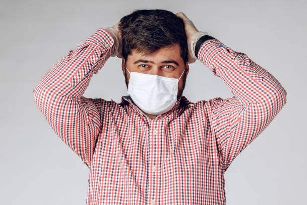 istock Sick man in medical mask on face and protective gloves on hands feeling headache. 1299164131