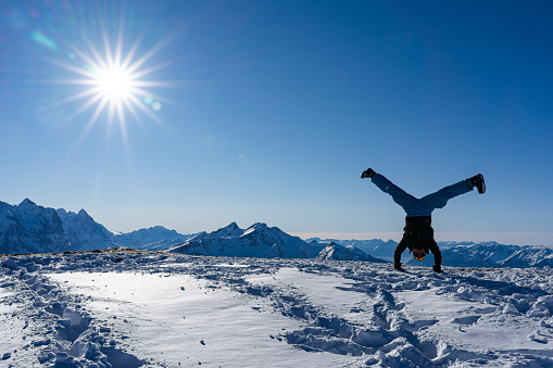 handstand straddle on snow caped mountain peak with blue sky and bright sunbeams. Copy space, concept.