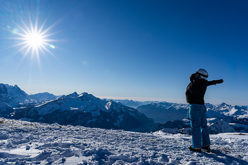 Girl enjoying sunbeams in winter with open arms at top of the mountain range. Snowboarder in late afternoon in the Swiss alps in winter. Spectacular view, for concept.