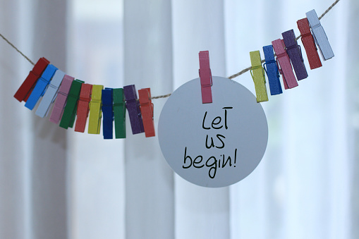 Let us begin. Inspirational motivational notes on tag label paper hanging on rope with colorful wooden clips decoration. Business action and life success successful concept.