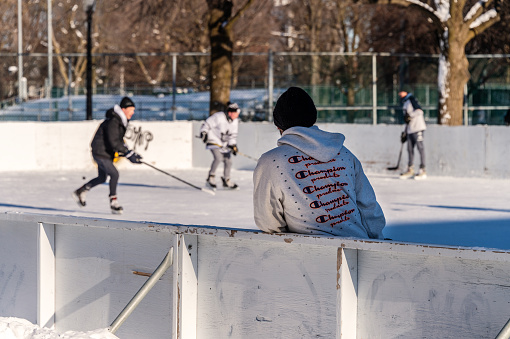 Montreal, CA - 24 January 2021: Young men playing hockey on outdoor ice rink in Lafontaine Park