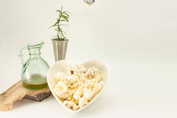 istock Popcorn isolated on white background served in heart shaped bowl accompanied by rosemary and olive oil 1299170913