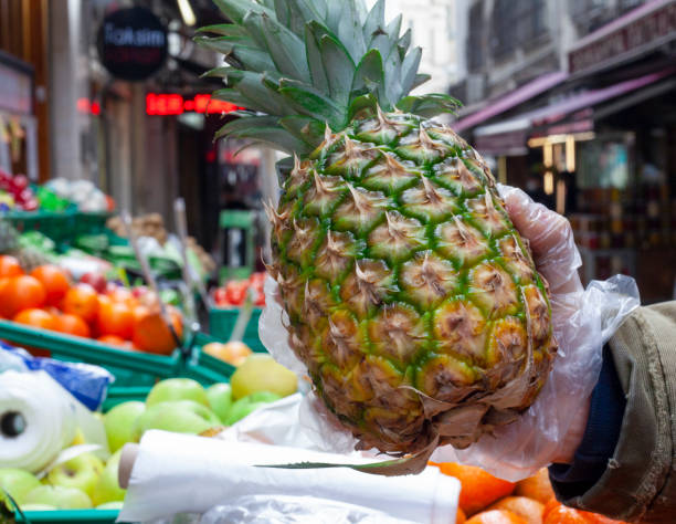 an asian fruit shop owner examining and choosing a good quality pineapple to his customer