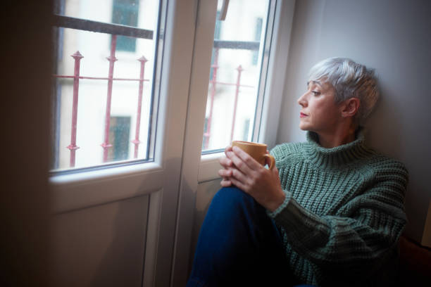 Senior woman sitting by the window drinking coffee