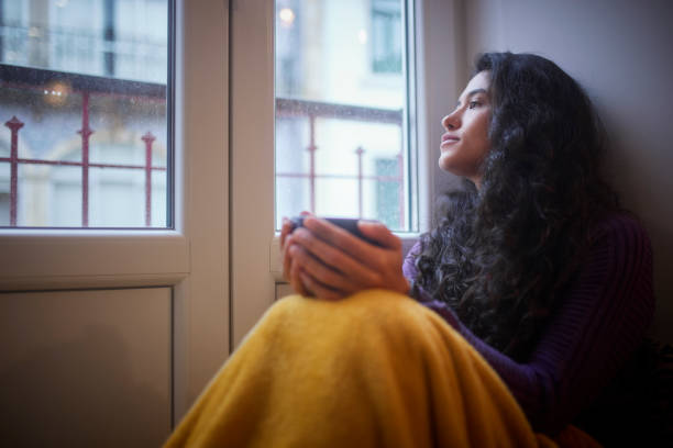 istock Latina woman sitting looking out the window drinking coffee 1299173136