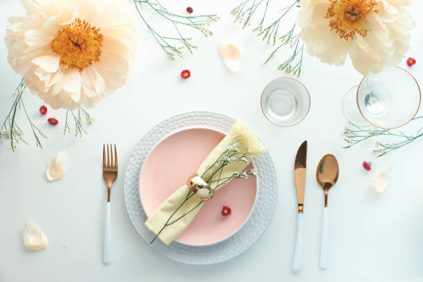 istock Effortless golden birthday dinner table decor. Pale yellow peony flowers. White dinner table, white and gold utensils, decorated with season flowers and palm leaves 1299173373
