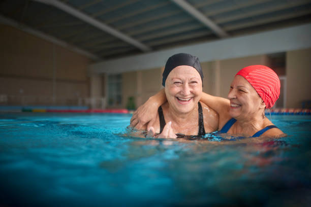 スイミングプールの屋内プールで一緒に抱き合う2人の先輩女性 - healthy lifestyle women jumping happiness ストックフォトと画像