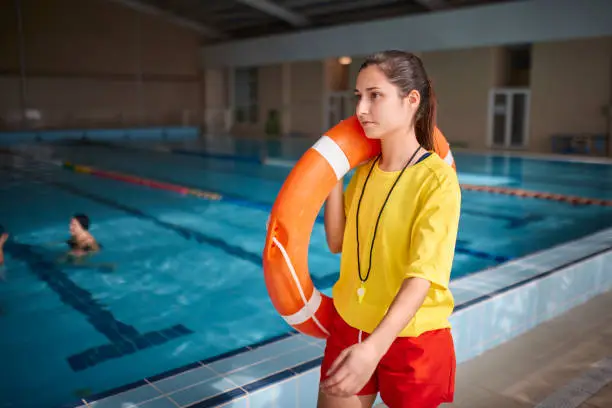 Close-up of female lifeguard walking with lifebuoy in indoor pool