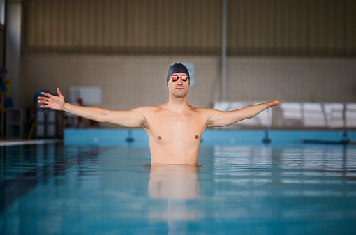 Disabled amputee swimmer arm stretching inside indoor pool with goggles and cap