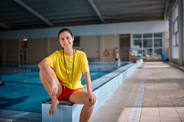 Portrait of female lifeguard smiling sitting on indoor pool side