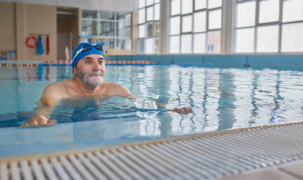 istock Senior man holding poolside exercising in indoor pool 1299174721